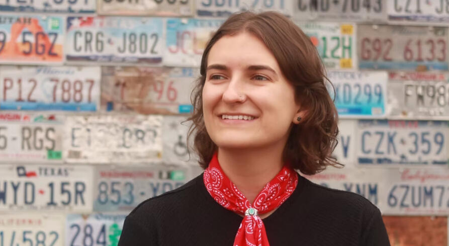 A photo of Gigs Hodges: a young woman with shoulder-length auburn hair wearing a red bandana round her neck, held by a turquoise ring